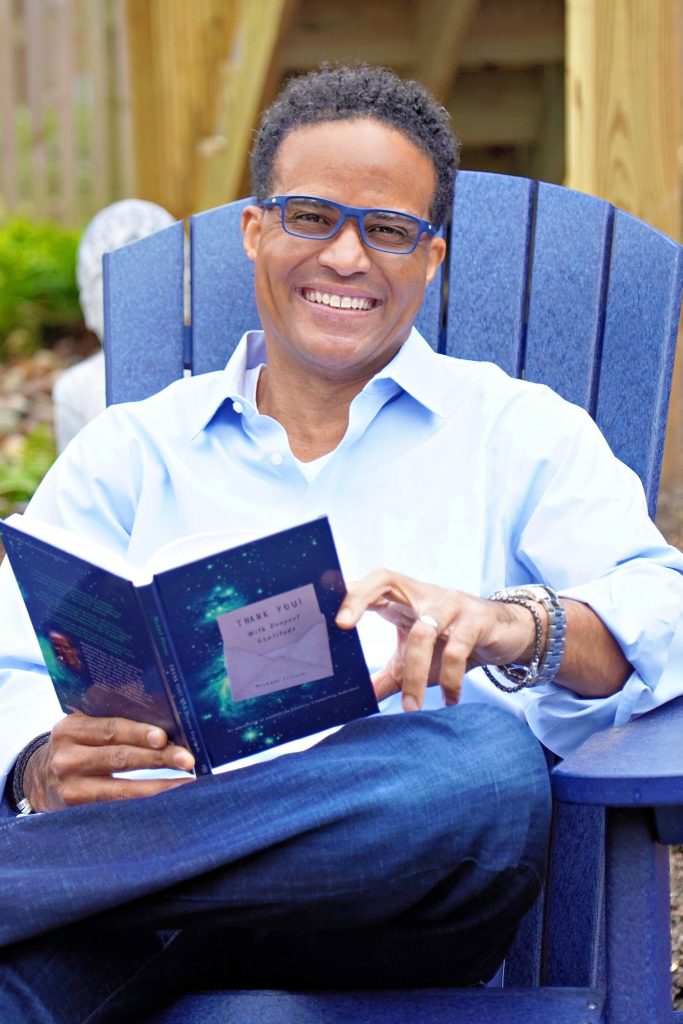 Author Michael Floissac seated outdoors with his book, "Thank You! With Deepest Gratitude"